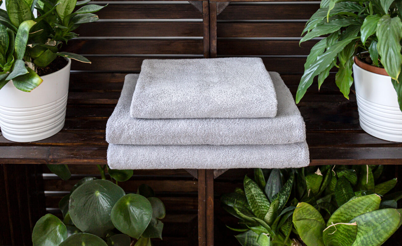 Bathroom set of folded gray towels in the craft made rough wooden shelf with plants