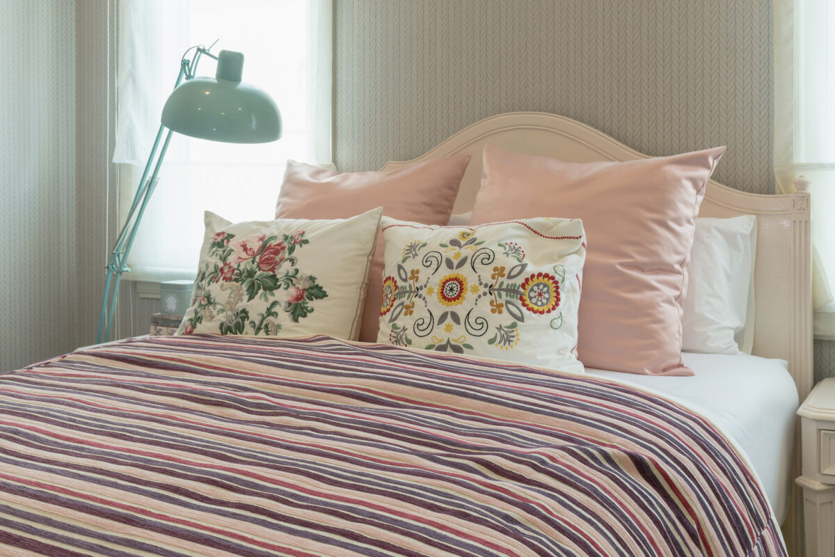 vintage bedroom interior with flower pillows and pink striped blanket on bed